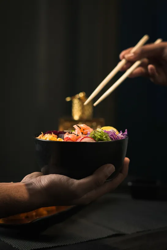 Hand presenting a poke bowl while chopsticks lift a bite