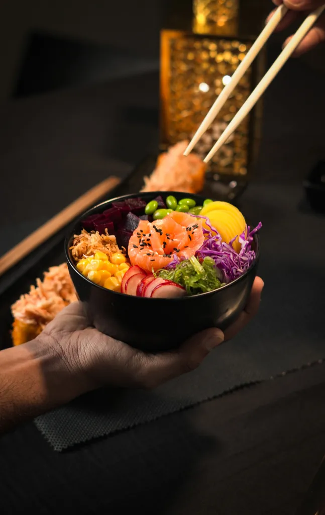 Close-up of a colourful poke bowl held in one hand with chopsticks above