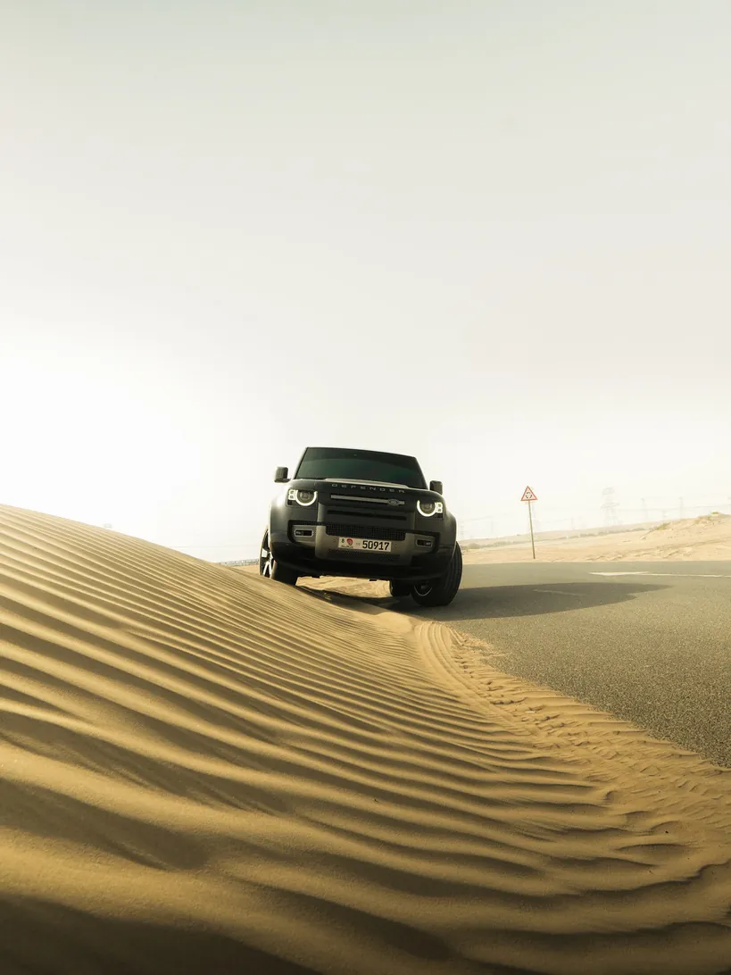 Dark SUV cresting rippled desert sand dunes