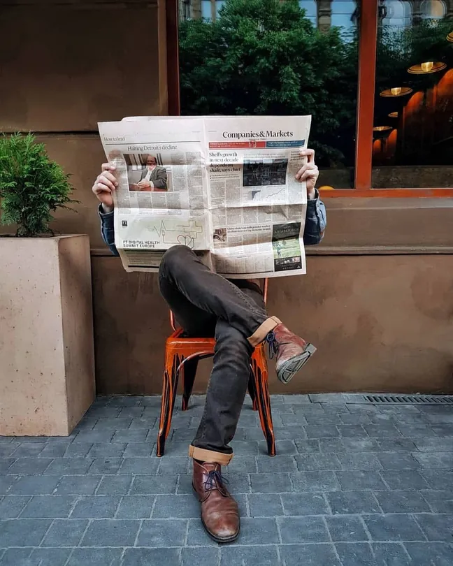 Person reading a newspaper on an orange chair outside a building