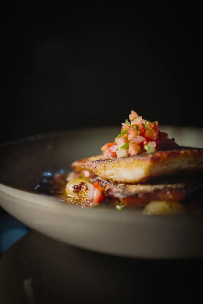 Seared fish topped with fresh salsa in a white bowl on a dark background