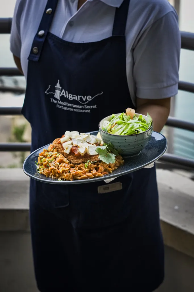 Server in an apron holding a plated rice dish and a salad