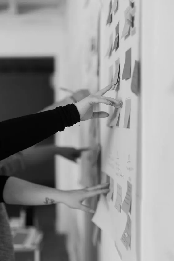 Hands arranging notes on a planning wall, black and white