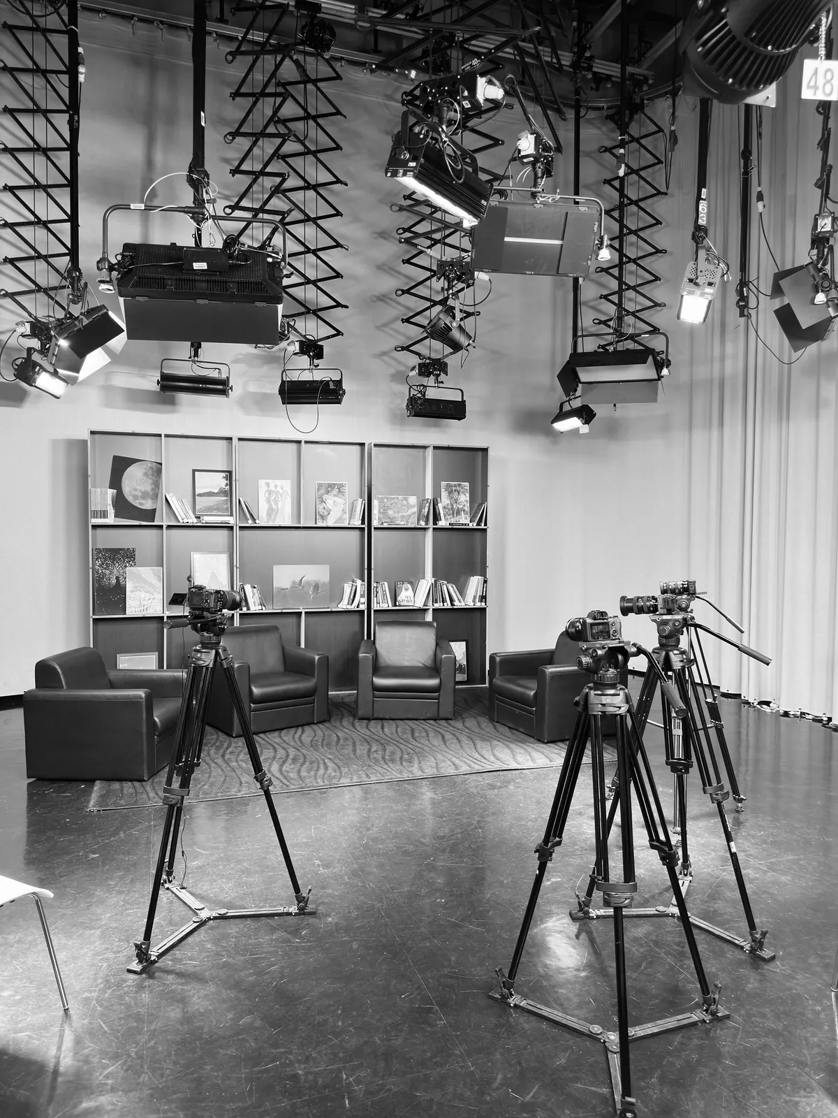 Black and white production studio with lighting rig, cameras on tripods and lounge chairs
