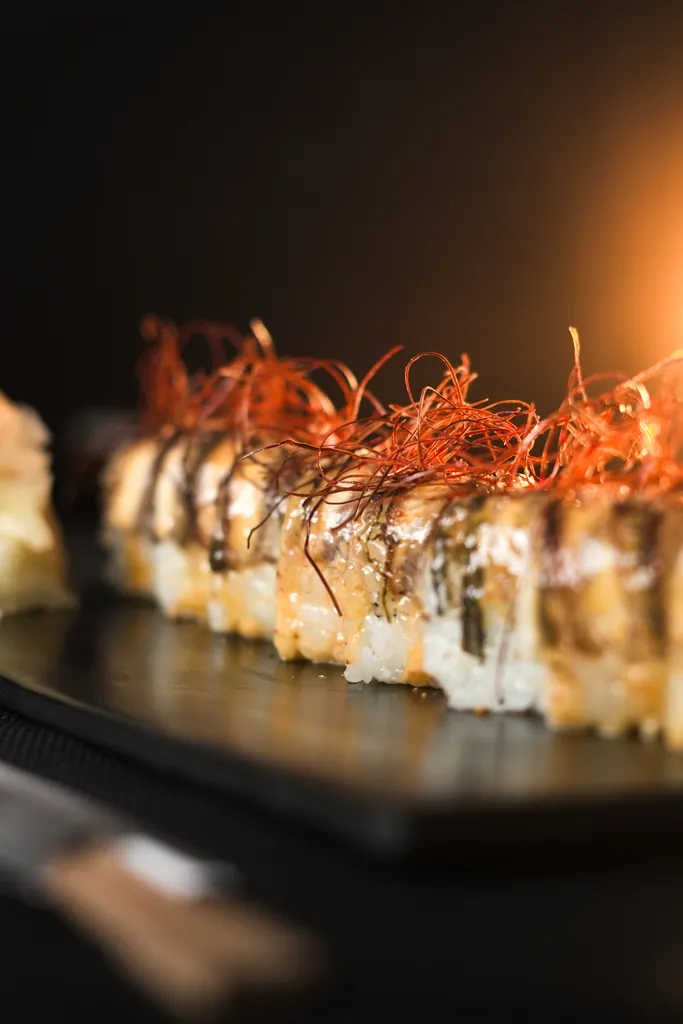 Row of seared sushi topped with crispy garnish against warm light
