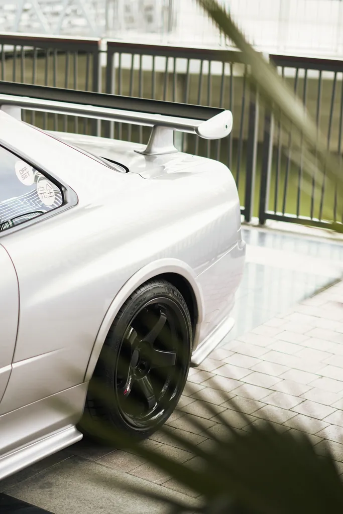 Side detail of a white sports coupe with a rear wing, framed by leaves